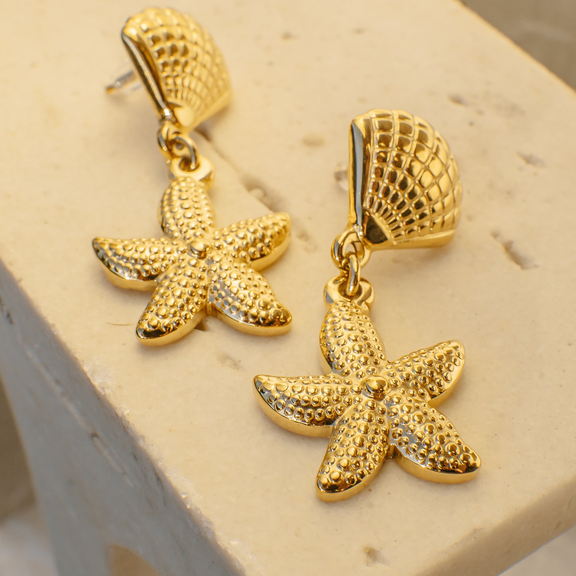 Gold starfish earrings on a beige background