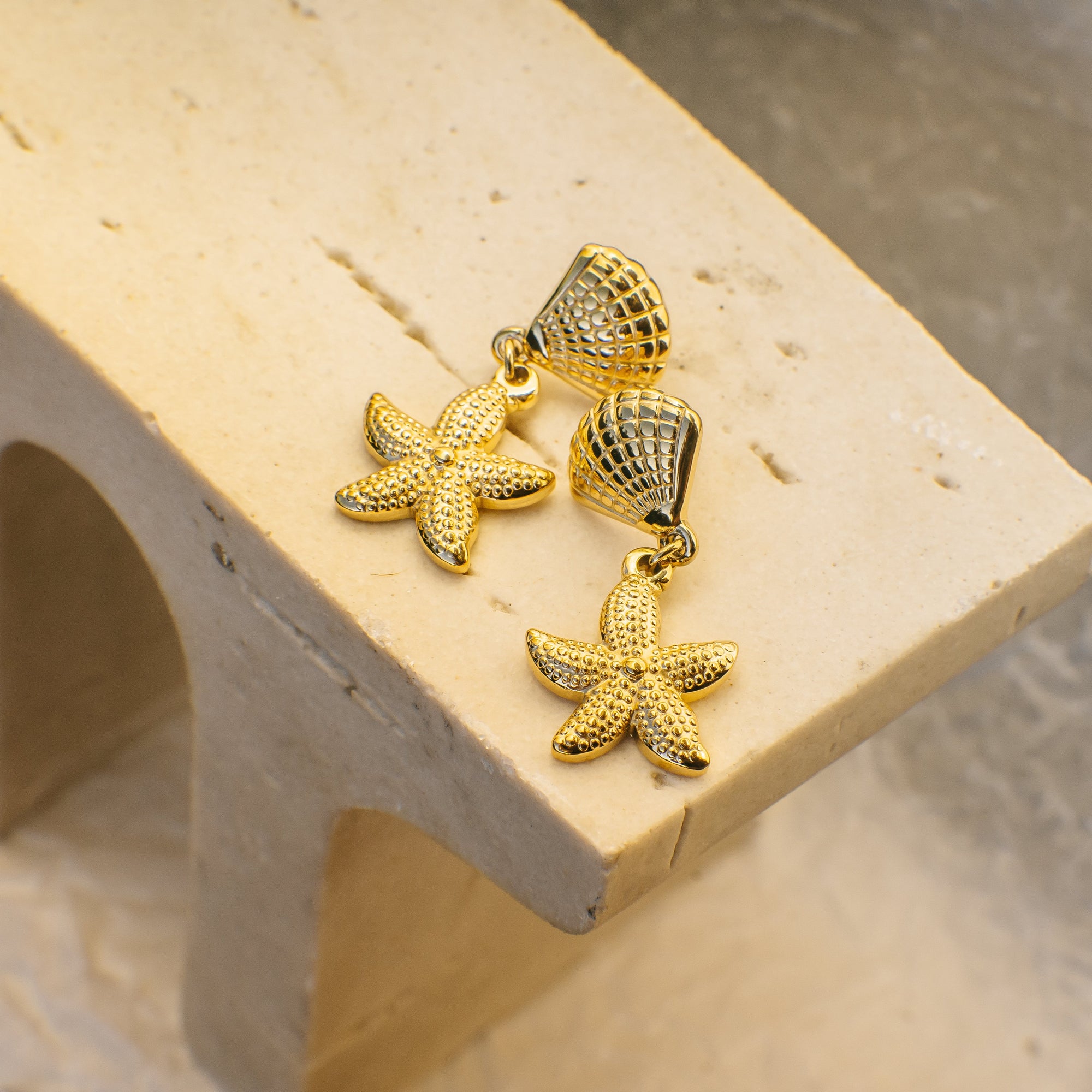 Gold starfish earrings on a beige stand with a neutral background